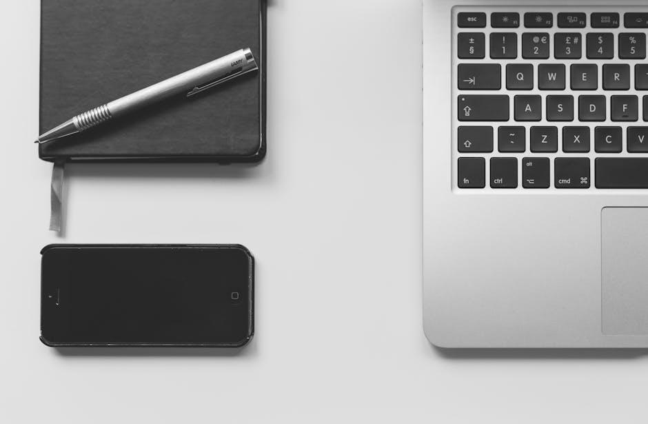 Modern minimalist workspace featuring a laptop, smartphone, and notebook on a desk.